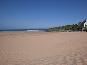 Ein weiter Sandstrand mit blauem Himmel, wenigen Personen und einem Gebäude mit steiler Dachform rechts.