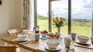 A dining table with breakfast items, a coffee maker, and a vase of flowers. - 2 Bed in Woolacombe (oc-43279) (Woolacombe)