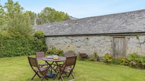 A stone building with a wooden door, surrounded by a grassy garden and a hedge. - 2 Bed in Woolacombe (oc-43279) (Woolacombe)