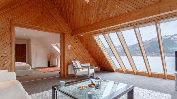 Ein geräumiges Loft mit hohen Decken, Holzbalken, einem Glastisch und Blick auf einen See.