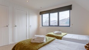 Ein Schlafzimmer mit zwei Betten, einem Fenster mit Blick auf Hügel und einem weißen Kleiderschrank.