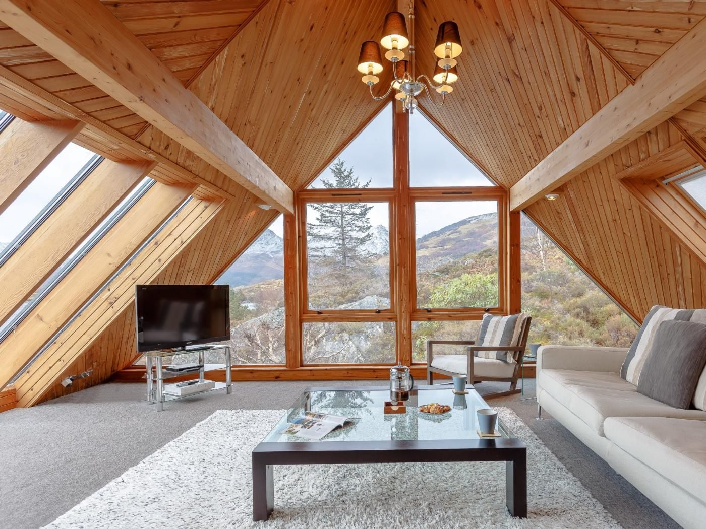 A high-ceilinged room with wooden beams, a glass coffee table, a sofa, and a TV.