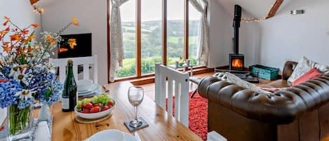 A cozy living room with a fireplace, a dining area with a table set for two, and a large window offering a scenic view.