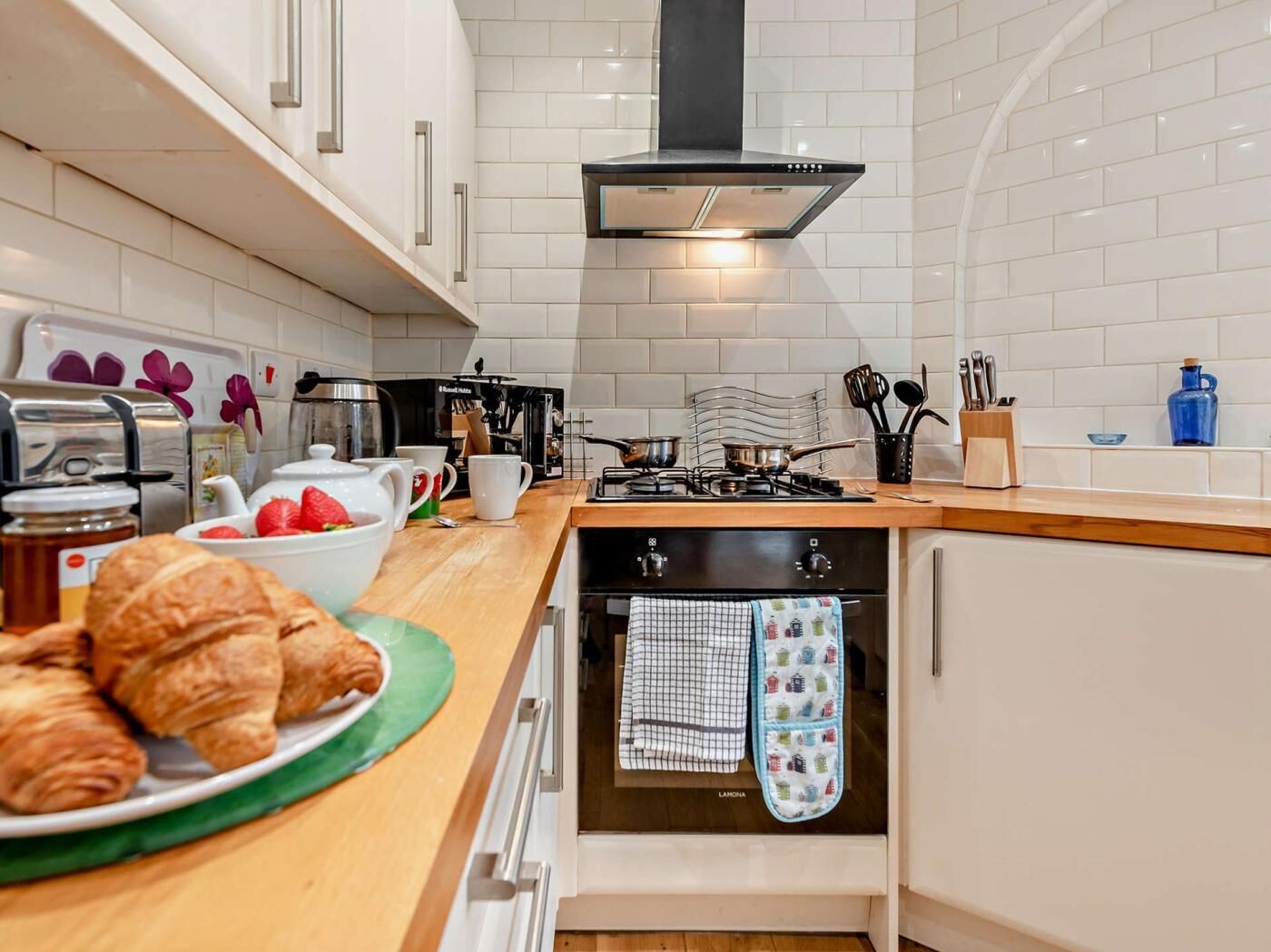 A modern kitchen with white cabinets, a gas stove, a black range hood, and a built-in oven.