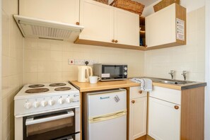 Eine kleine Küchenzeile mit Herd, Mikrowelle, Kühlschrank und Spüle.