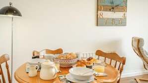 Une table à manger dressée avec des aliments pour le petit-déjeuner, une horloge au mur et une lampe sur pied.