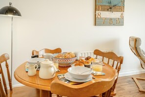 Ein Esstisch, gedeckt mit Frühstücksleckereien, eine Uhr an der Wand und eine Stehlampe.