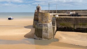 Une scène côtière avec une plage de sable, une structure en pierre et un bateau au loin.