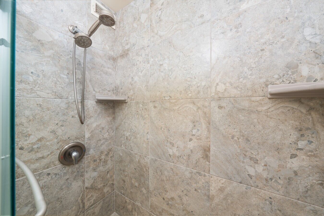 A shower with a handheld showerhead and a wall-mounted control panel.