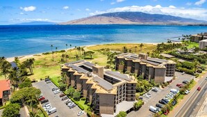 Un hotel costero con varias construcciones, un estacionamiento y vistas al océano y una montaña al fondo.