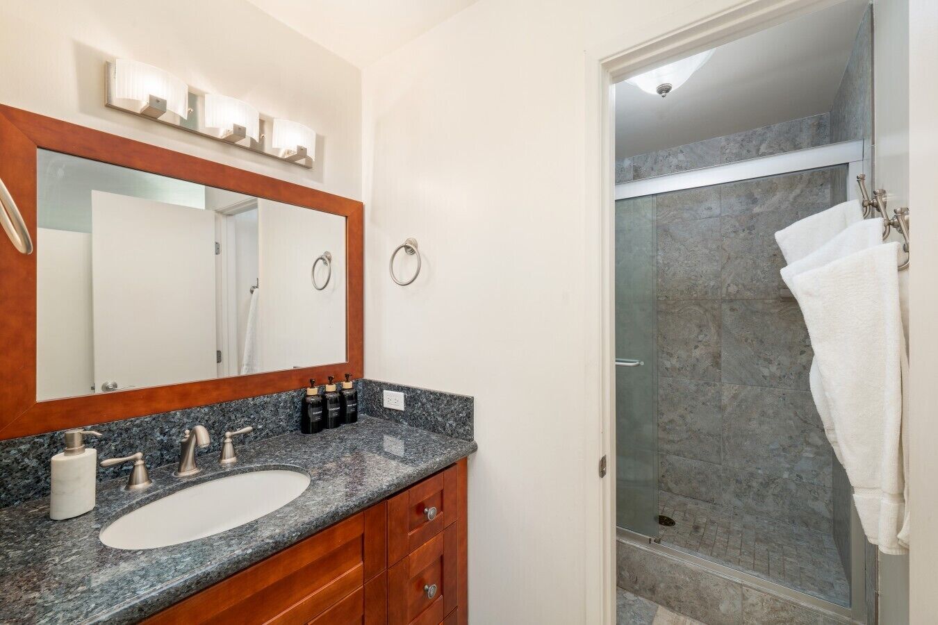 Un baño con lavamanos de mármol, un espejo grande y cabina de ducha con paredes de vidrio.