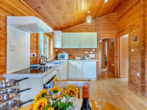 A wooden cabin interior with a kitchen, dining area, and a visible door leading to another room.