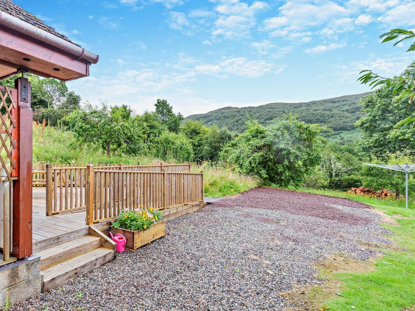 A wooden deck with steps leading to a building, a gravel area, and a view of a forested hillside.