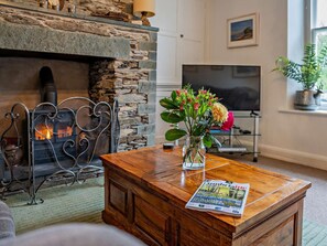 Ein gemütliches Wohnzimmer mit Kamin aus Stein, einem Couchtisch aus Holz mit einer Zeitschrift, einem Fernseher und einer Zimmerpflanze.