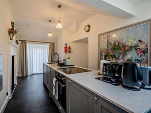 A modern kitchen with a central island, a coffee machine, and a painting of flowers on the wall. - 2 Bed in Ulverston (oc-94926) (Lakeside)