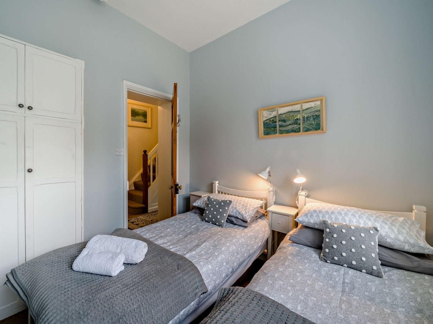Een slaapkamer met twee eenpersoonsbedden, een kledingkast, een schilderij aan de muur en een trap naar een andere kamer.
