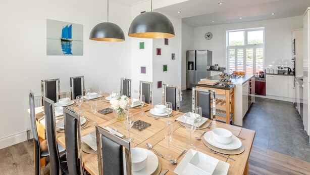 Un comedor moderno con una amplia mesa de madera, sillas negras e iluminación colgante.