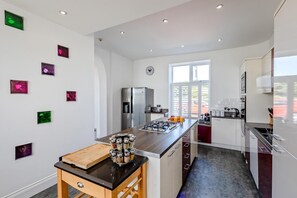 A modern kitchen with a central island, stainless steel appliances, and a window providing natural light. - 6 Bed in Bideford (oc-beaho) (Bideford)