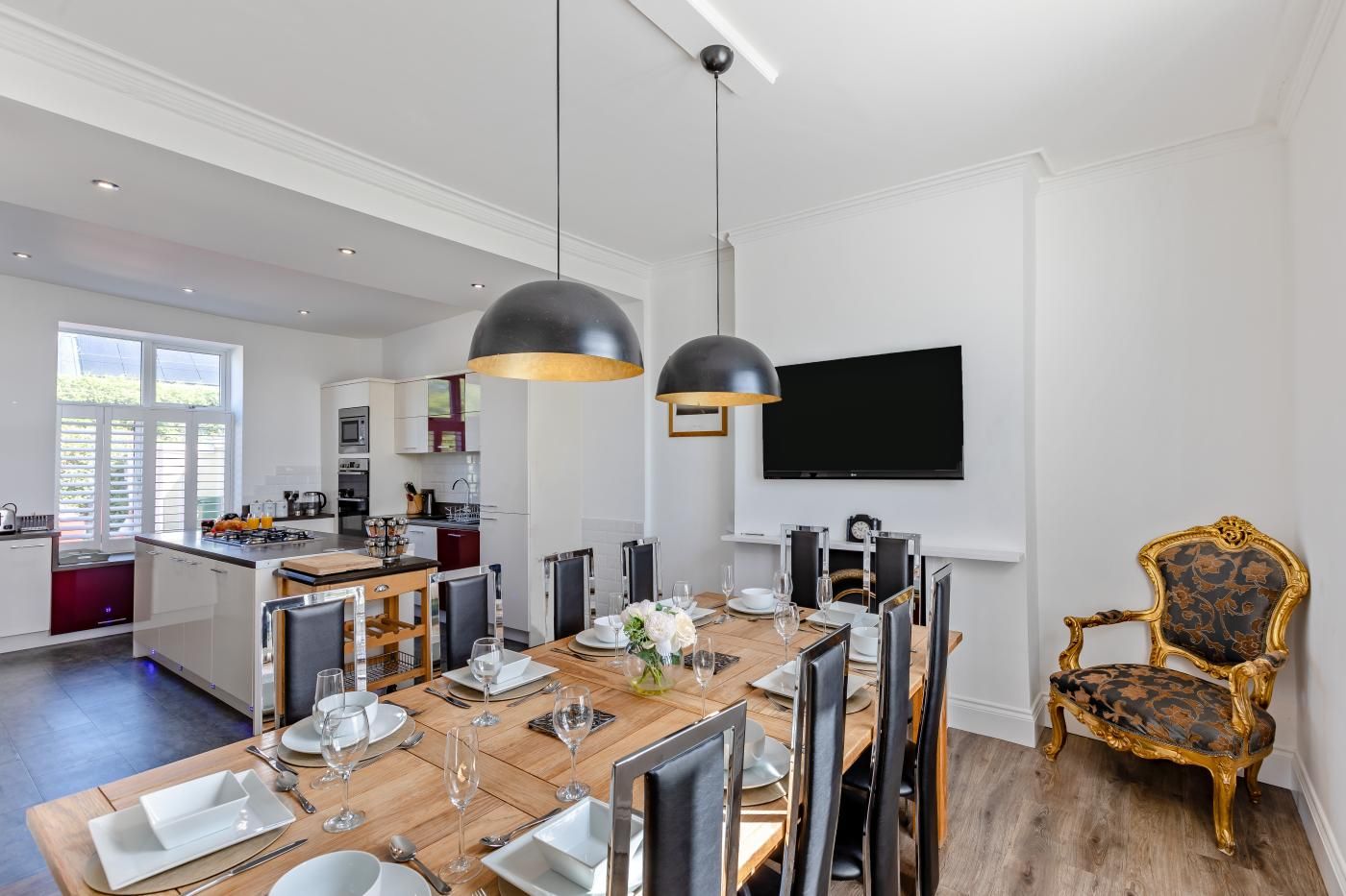 A modern kitchen with a dining area, a flat-screen TV mounted on the wall, and a classic chair with ornate detailing.