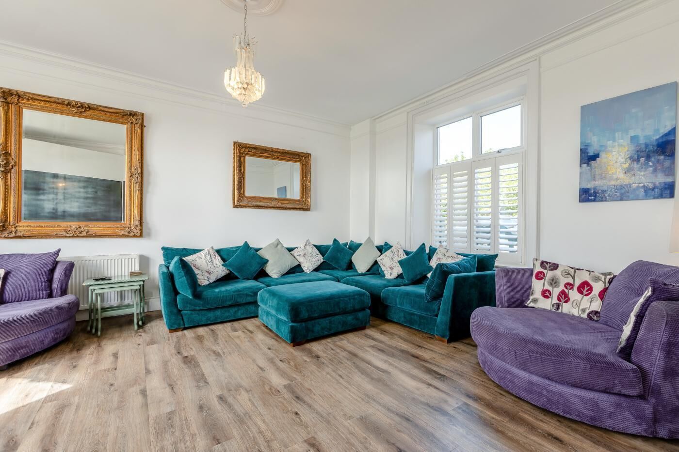 A living room with a teal sectional sofa, a purple armchair, a small table, and a large mirror.