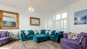 Una sala de estar con un sofá seccional color turquesa, un sillón púrpura, una mesita y un espejo grande.