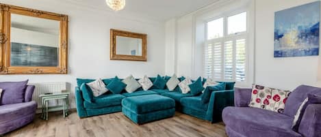 Una sala de estar con un sofá seccional color turquesa, un sillón púrpura, una mesita y un espejo grande.