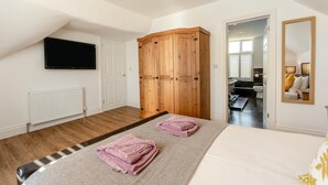 Un dormitorio con cama, un armario de madera, televisión y un baño visible a través de una puerta abierta.