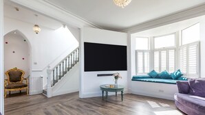 Una sala de estar con escalera, televisor de pantalla plana, una mesa redonda con un florero y un sofá.