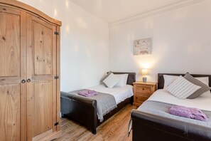 A room with two beds, a wooden wardrobe, a nightstand with a lamp, and a wall-mounted artwork. - 6 Bed in Bideford (oc-beaho) (Bideford)