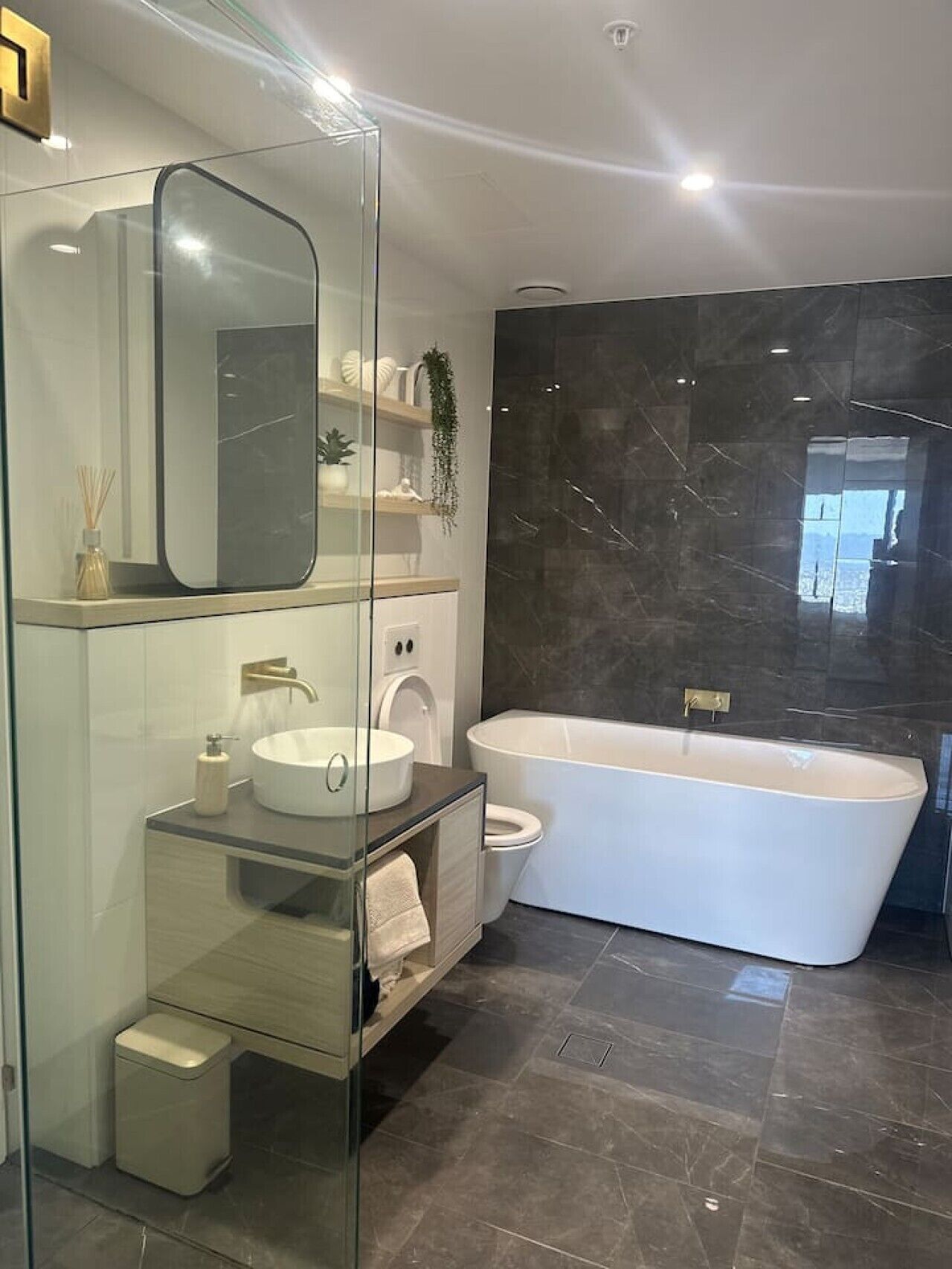 Et moderne badeværelse med et fristående badekar, en glasafskærmet brusekabine og et toiletbord med vask og spejl.