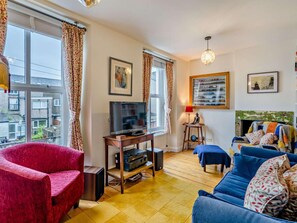 Ein Wohnzimmer mit Fernseher, einem roten Sessel, einem blauen Sofa und einem Kamin.
