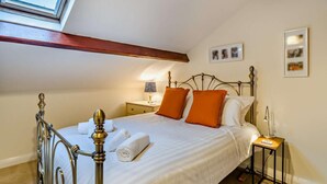 Una camera da letto con un lucernario, un letto con lenzuola bianche e cuscini arancioni, un comodino con una lampada e un tavolino anch'esso con una lampada.