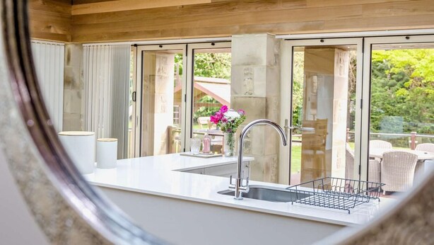 A modern kitchen with a large window, a sink, and a dining area visible through the glass doors. - 1 Bed in Alnwick (oc-94771) (Alnwick)