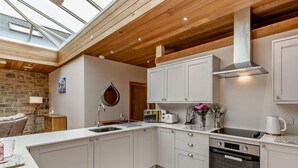 A modern kitchen with a skylight, wooden ceiling beams, and a stone wall. - 1 Bed in Alnwick (oc-94771) (Alnwick)