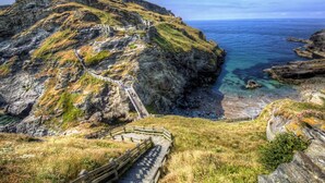 Eine Küstenlandschaft mit einem felsigen Klippen, einer hölzernen Treppe, die nach oben führt, und freiem Blick auf das Meer.