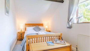 Ein Schlafzimmer mit Bett, Nachttischen, einer Holzbank, einem Heizkörper und einem Fenster mit Vorhängen.