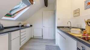 Eine moderne Küche mit Dachfenster, weißen Schränken, einem Einbauofen und einer Arbeitsplatte mit Küchenutensilien.