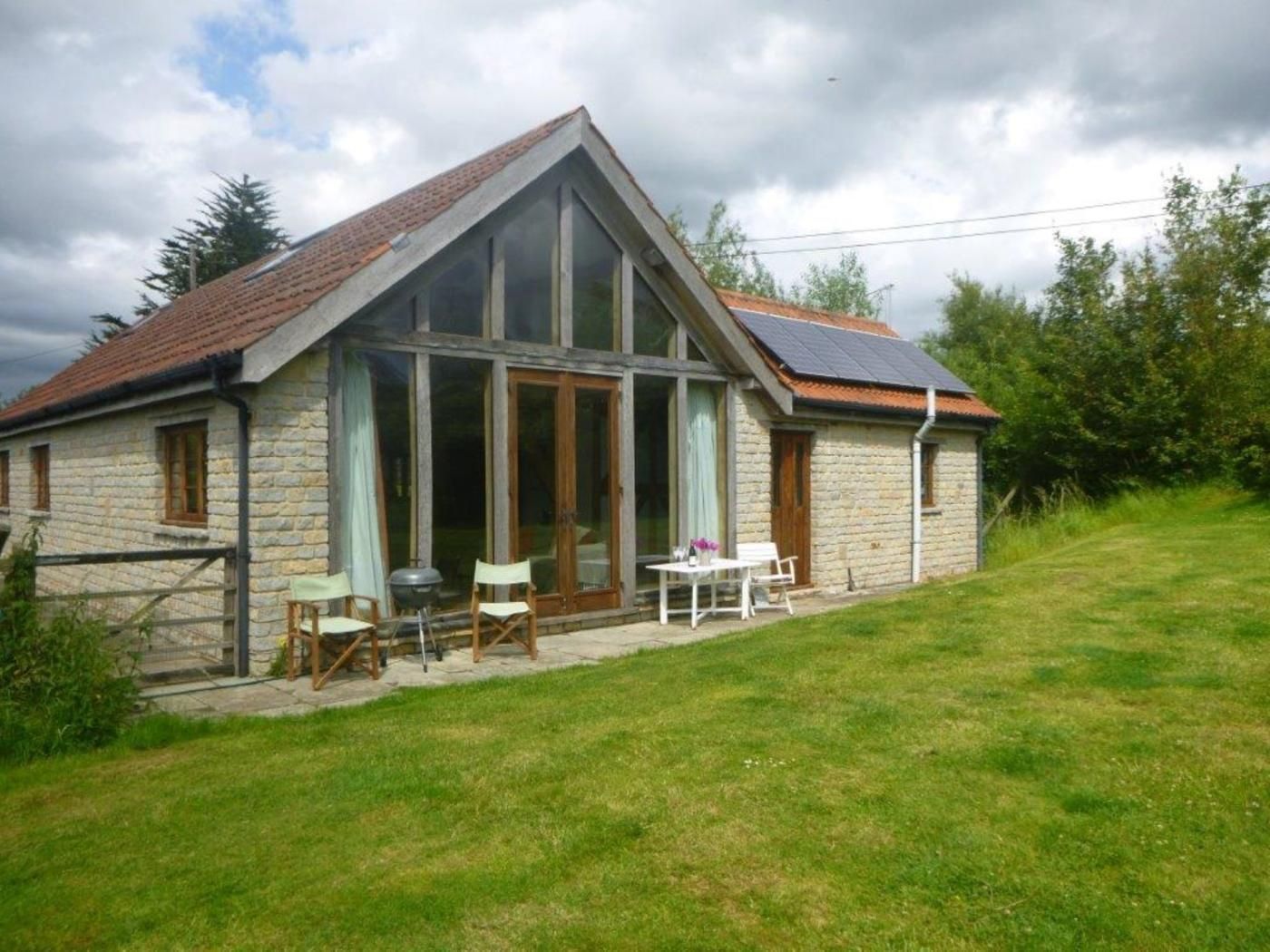 A stone house with a sloped roof, large windows, and a patio with outdoor furniture.