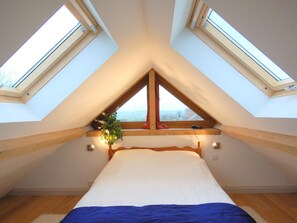 A bedroom with a sloped ceiling and skylights, a bed with a blue blanket, and a window with a plant. - 1 Bed in Somerton (oc-asher) (Compton Dundon)