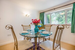 A dining area with a glass table, four chairs, a vase of red flowers, and a window with curtains. - 1 Bed in Ringwood (oc-50147) (Ashley Heath)