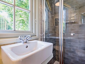 A bathroom with a white sink, a glass shower enclosure, and a window with a view of greenery. - 1 Bed in Fowey (oc-95015) (Golant)