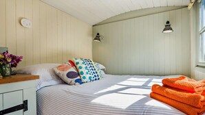 A bedroom with a bed, pillows, a nightstand, a vase with flowers, and a window. - 1 Bed in Fowey (oc-95015) (Golant)