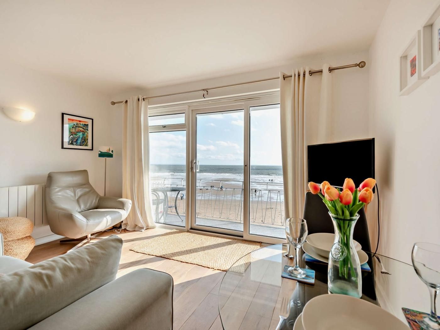 A modern living room with a large sliding glass door leading to a beach view.