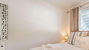Habitación de hotel con cama, mesita de noche con lámpara, espejo en la pared y ventana con cortinas.