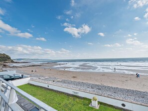 Ein Strand mit einer Grünfläche im Vordergrund, blauem Himmel und dem Meer im Hintergrund.