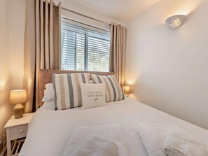 A hotel room with a bed, curtains, a nightstand, a lamp, and a wall-mounted light fixture. - 1 Bed in Saundersfoot (oc-48140) (Saundersfoot)