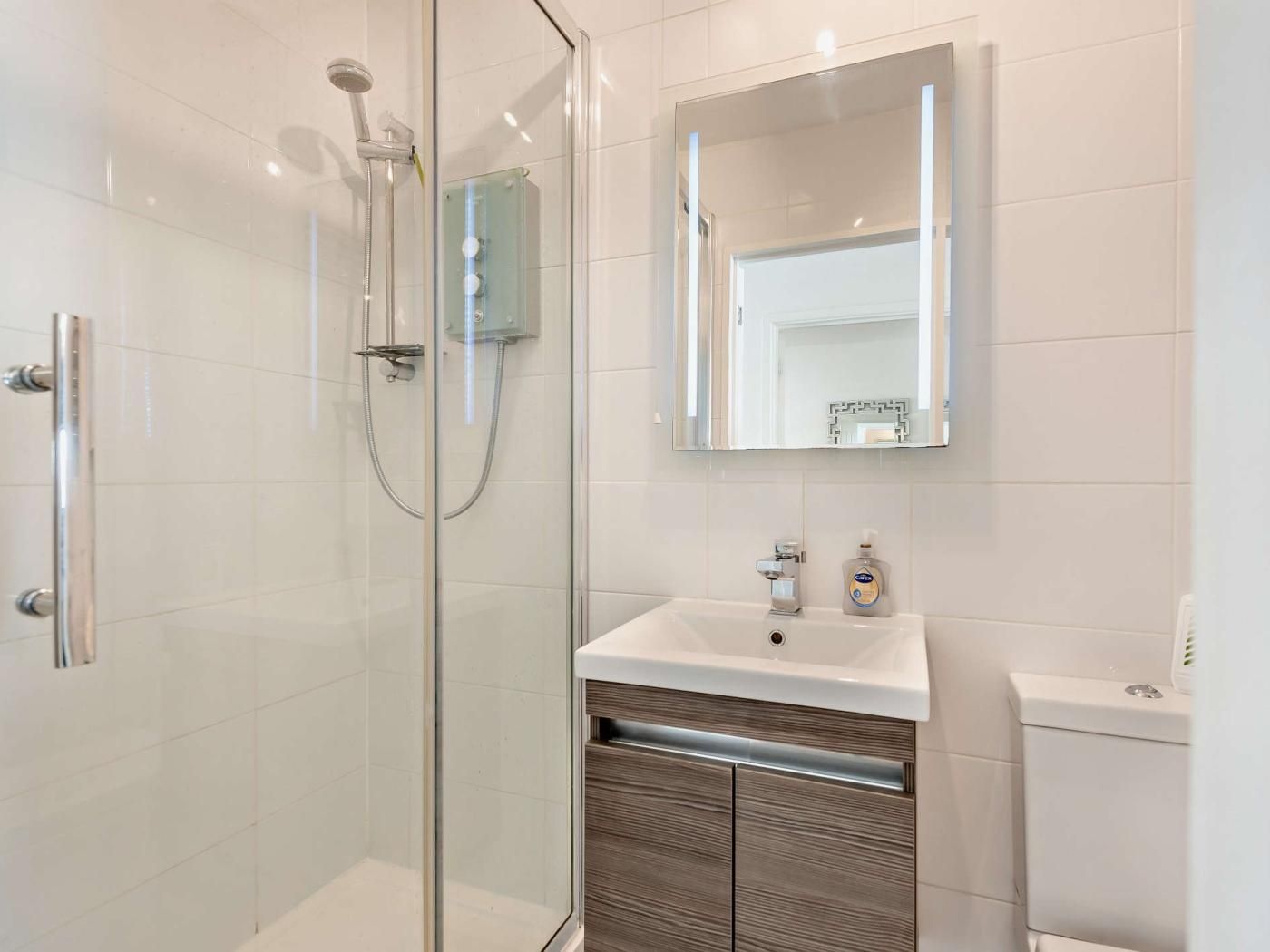 Ein modernes Badezimmer mit Duschkabine aus Glas, einem weißen Waschbecken mit Spiegel darüber und einer Toilette.
