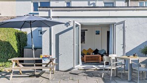 Une maison moderne dotée d’un patio comprenant une table en bois, des chaises et un parasol.