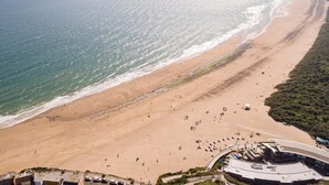 Une plage avec une longue étendue de sable, quelques personnes et un bâtiment doté d’un toit incurvé.