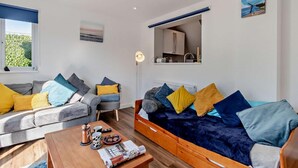 Un salon moderne comprenant un canapé, un fauteuil et une table basse, une lucarne, une vue sur l’extérieur et un coin cuisine.